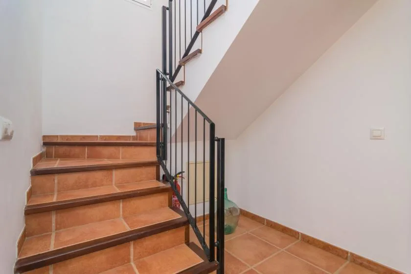 A tiled staircase with a black metal railing rises along a white wall.