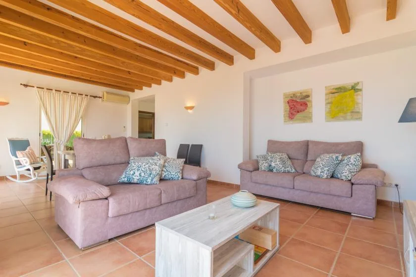 A living room with two seating areas, a coffee table, and exposed wooden ceiling beams.