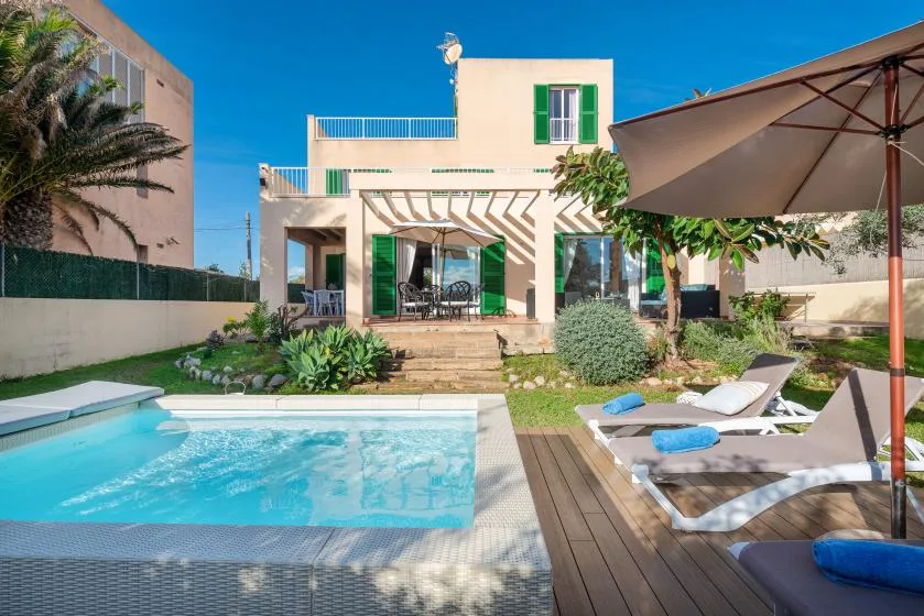 A modern house overlooks a swimming pool and patio seating.