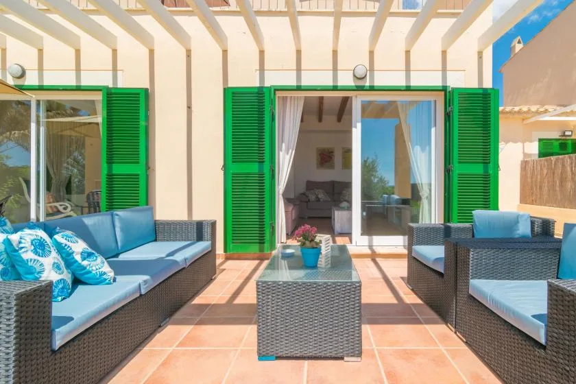 A sunlit patio with cushioned seating, green shutters, and a glass doorway.