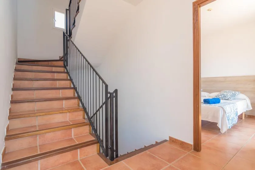A tiled staircase with a dark railing rises beside an open bedroom doorway.