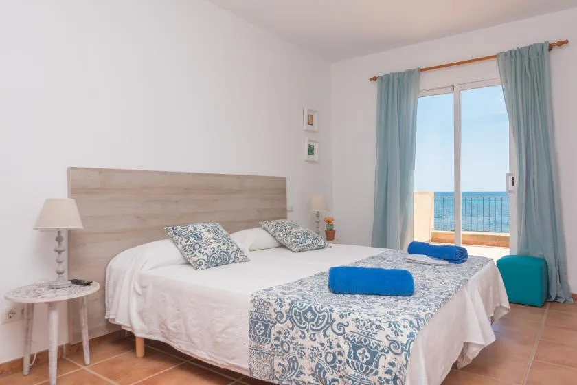 A bright bedroom with a double bed and blue curtains beside a balcony door.