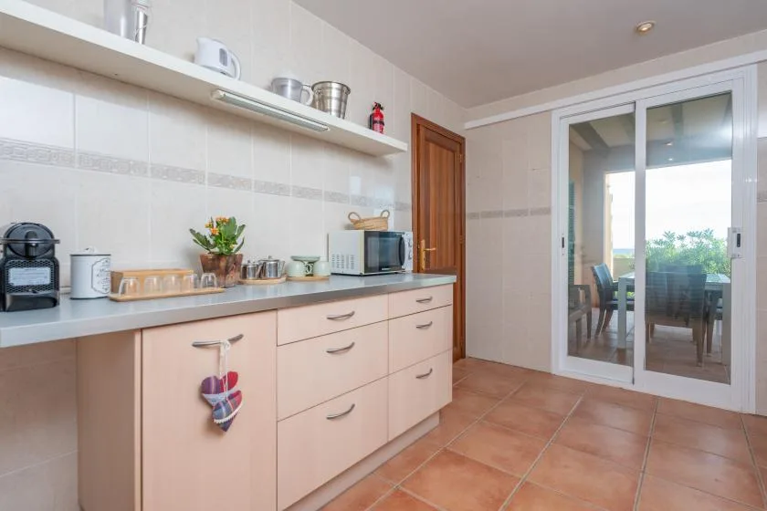 A tiled kitchen with a countertop, cabinets, and sliding glass doors opening onto a patio.