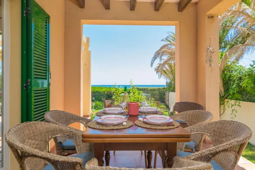 A covered patio dining area with a table and woven seating overlooking the sea.