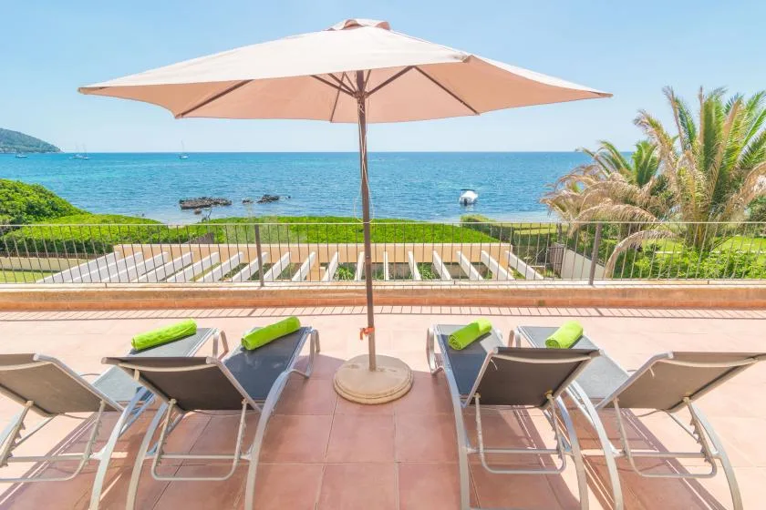 A seaside terrace with lounge seating and a large sun umbrella overlooking the water.