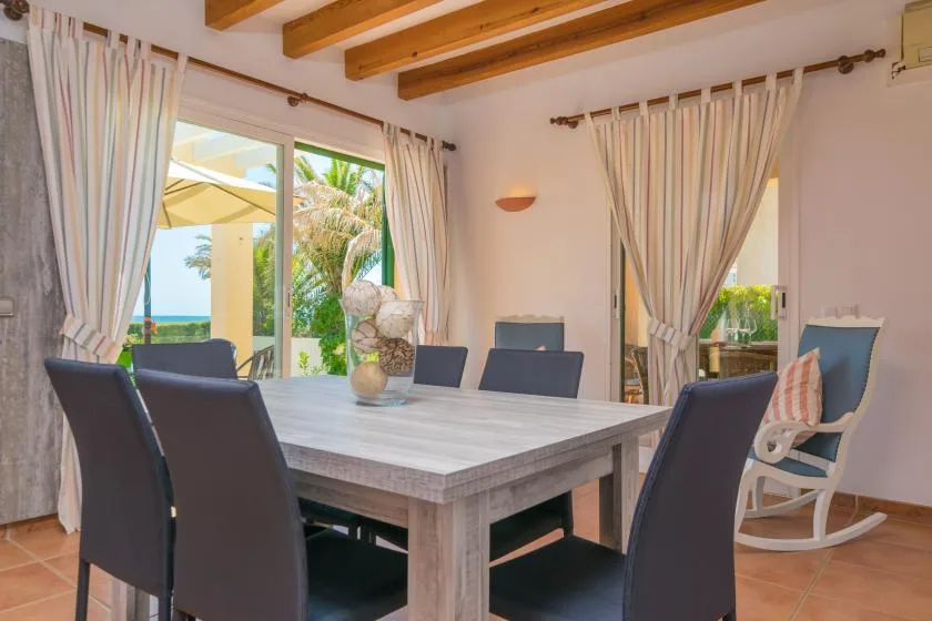 A dining area with a long table and chairs beside curtained windows.
