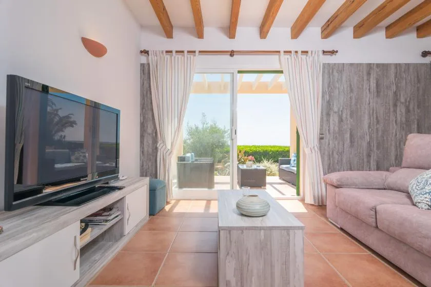 A bright living room with seating, a television, and glass doors opening onto greenery.