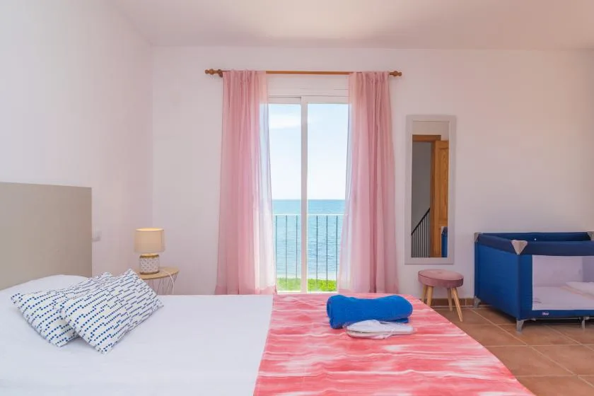 A bedroom with a bed, pink curtains, and a window overlooking the sea.