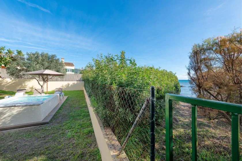 A fenced outdoor pool area sits beside greenery, with a glimpse of water beyond.