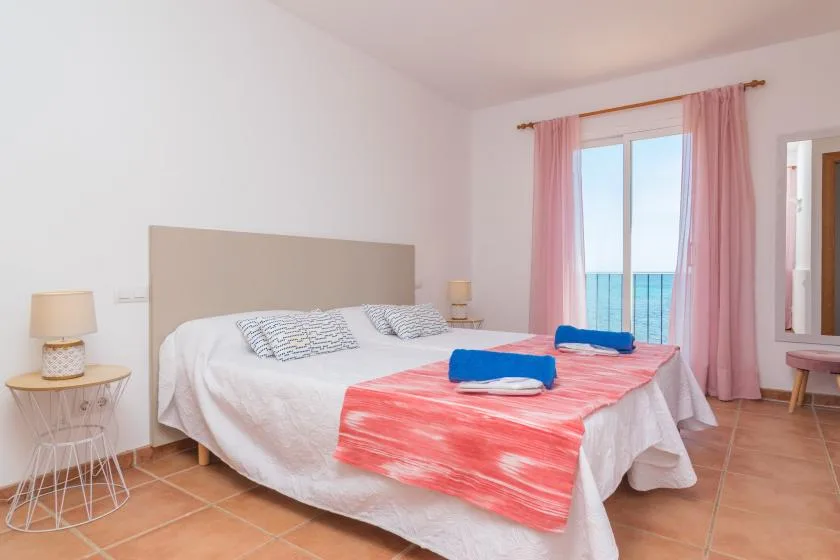 A bedroom with a bed dressed in white and coral linens beside a window.