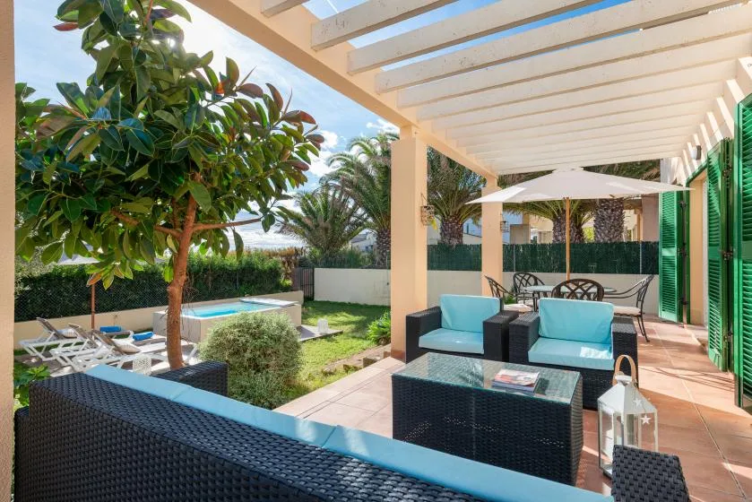 A covered patio with outdoor seating overlooks a garden and swimming pool.