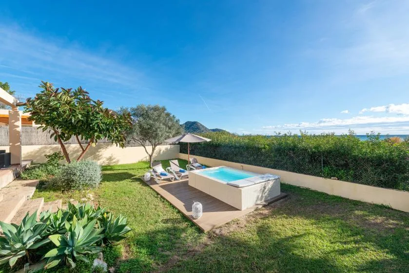 A garden patio with a small pool, umbrella, and surrounding greenery.