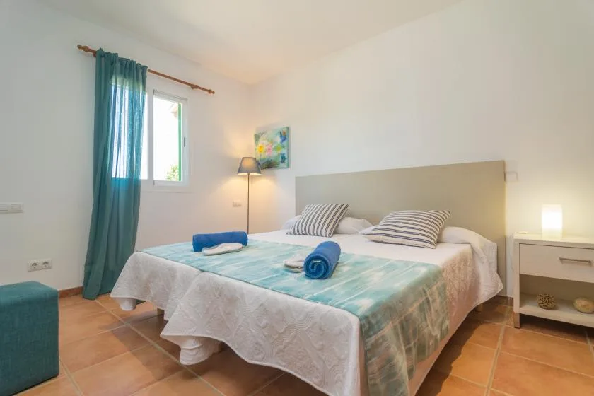 A bright bedroom with a bed dressed in white and teal bedding.