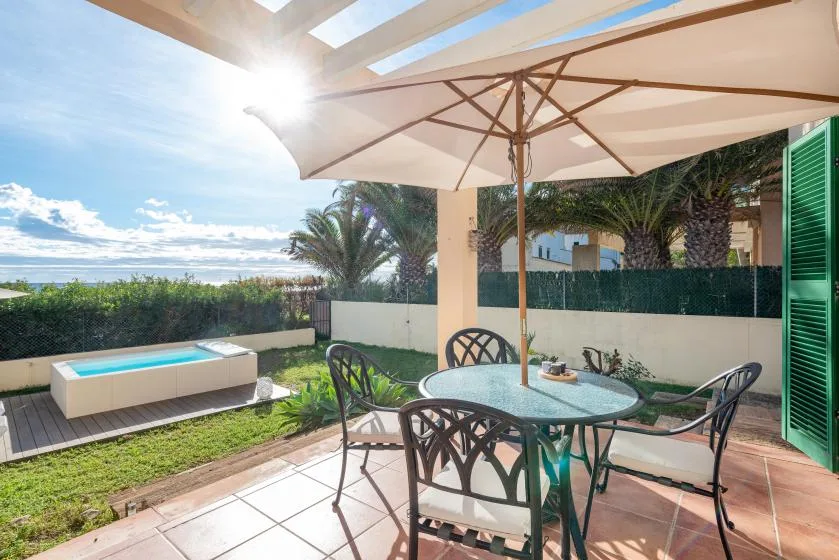 A sunny patio with a round outdoor table, seating, and a large umbrella.