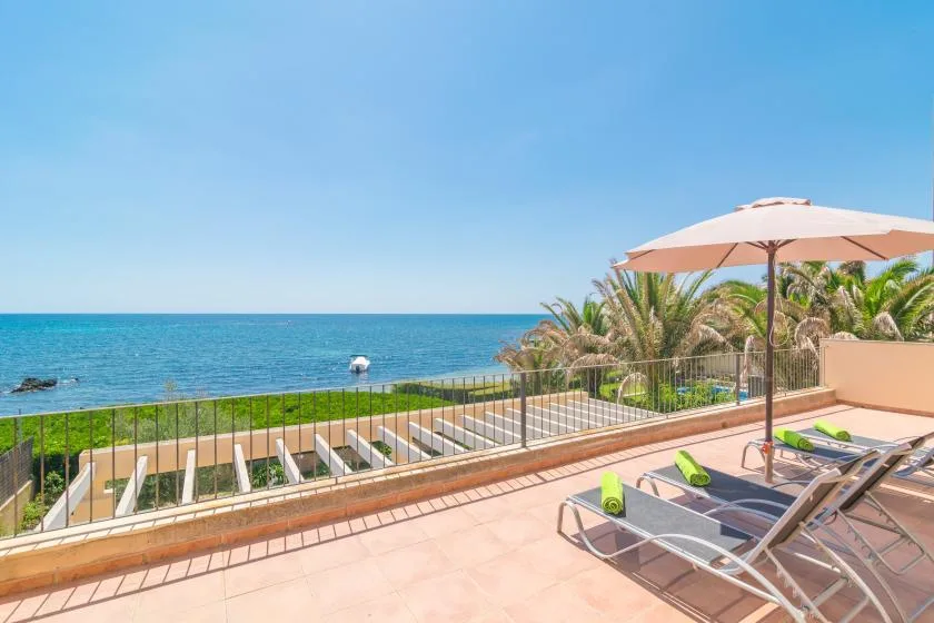 A seaside terrace overlooks the ocean, with sun loungers beneath a parasol.