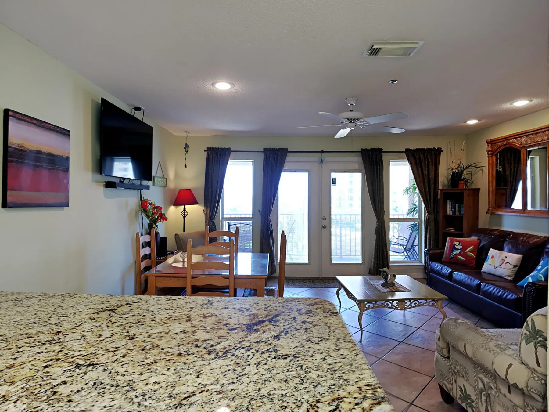 A living room with a dining table, seating, and windows opening onto a balcony.