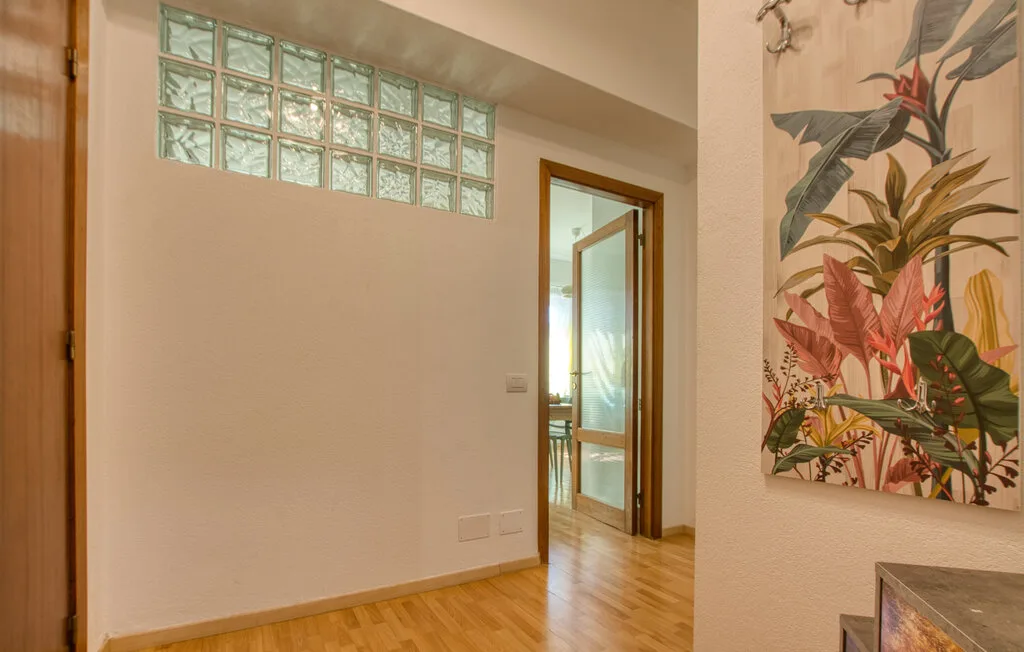 Un pasillo con suelo de madera, ventanas de bloques de vidrio y una gran obra botánica.