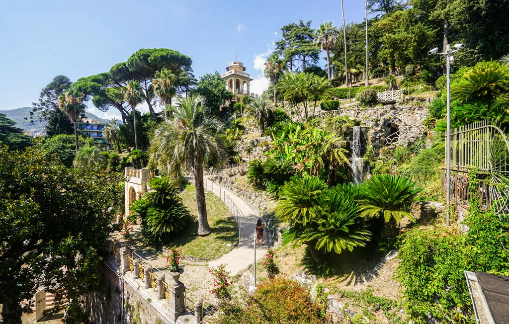 Un jardín paisajístico con senderos de piedra, plantas frondosas y árboles en un día soleado.