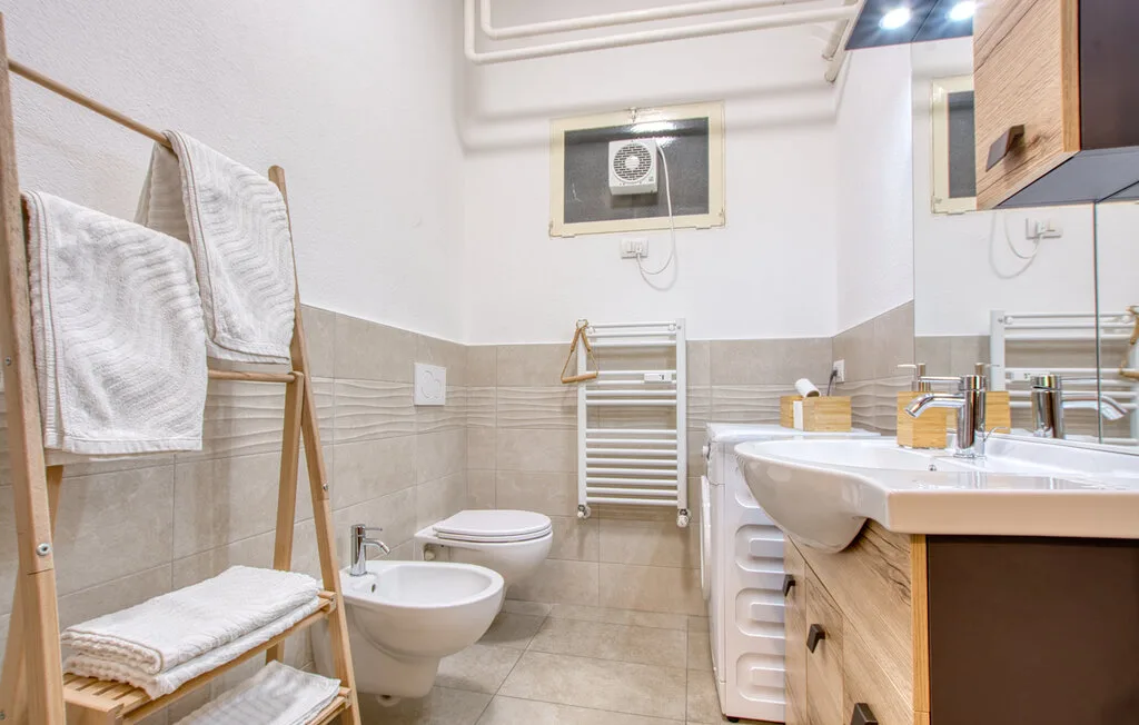 Un baño con lavabo, inodoro y toallas en un estante de madera.