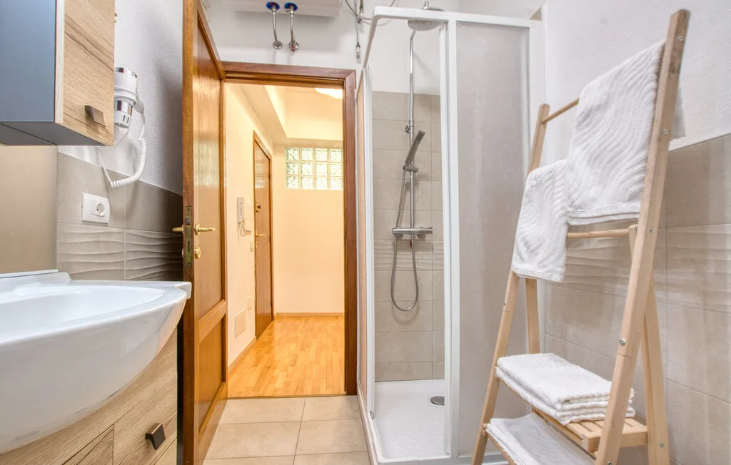 Un baño con lavabo, ducha y toallas sobre un soporte de madera.