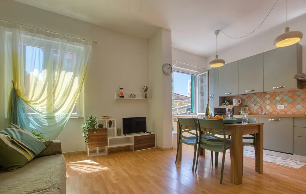 Una luminosa sala-comedor de planta abierta con cocina y una gran ventana con cortinas.