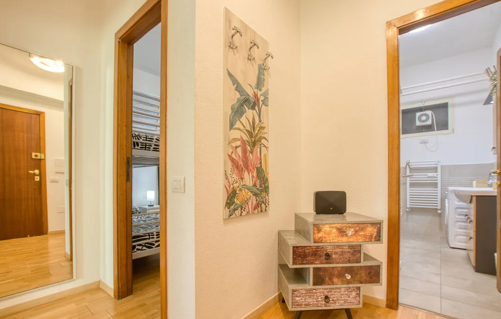 Un pasillo luminoso con un pequeño mueble decorativo y puertas abiertas.