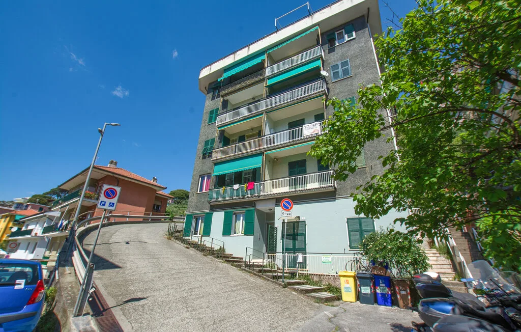 Un edificio de apartamentos con balcones se alza junto a una calle pavimentada en pendiente.