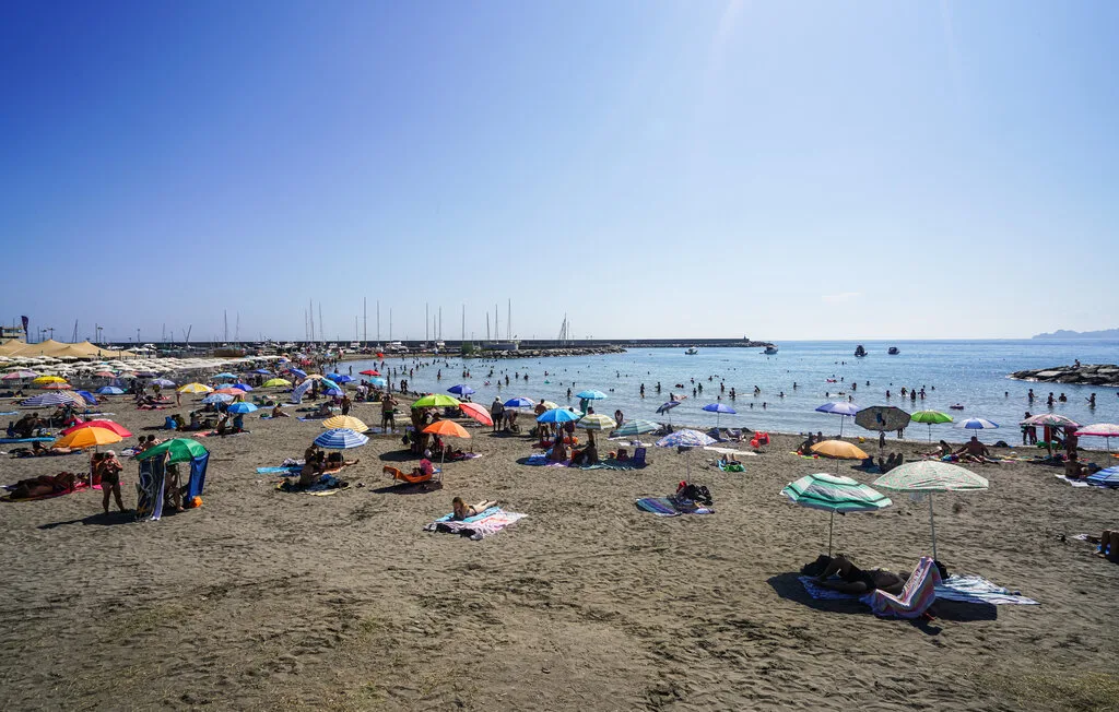 Una playa concurrida con sombrillas coloridas y personas bañándose en el mar.