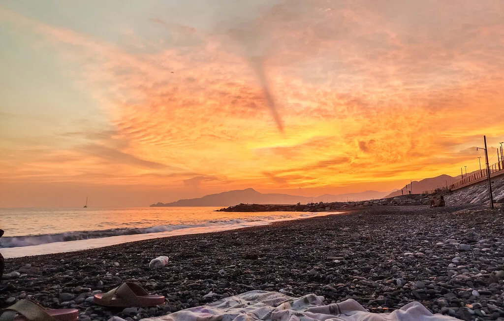 Una playa de guijarros al atardecer, con olas suaves bajo un cielo colorido.