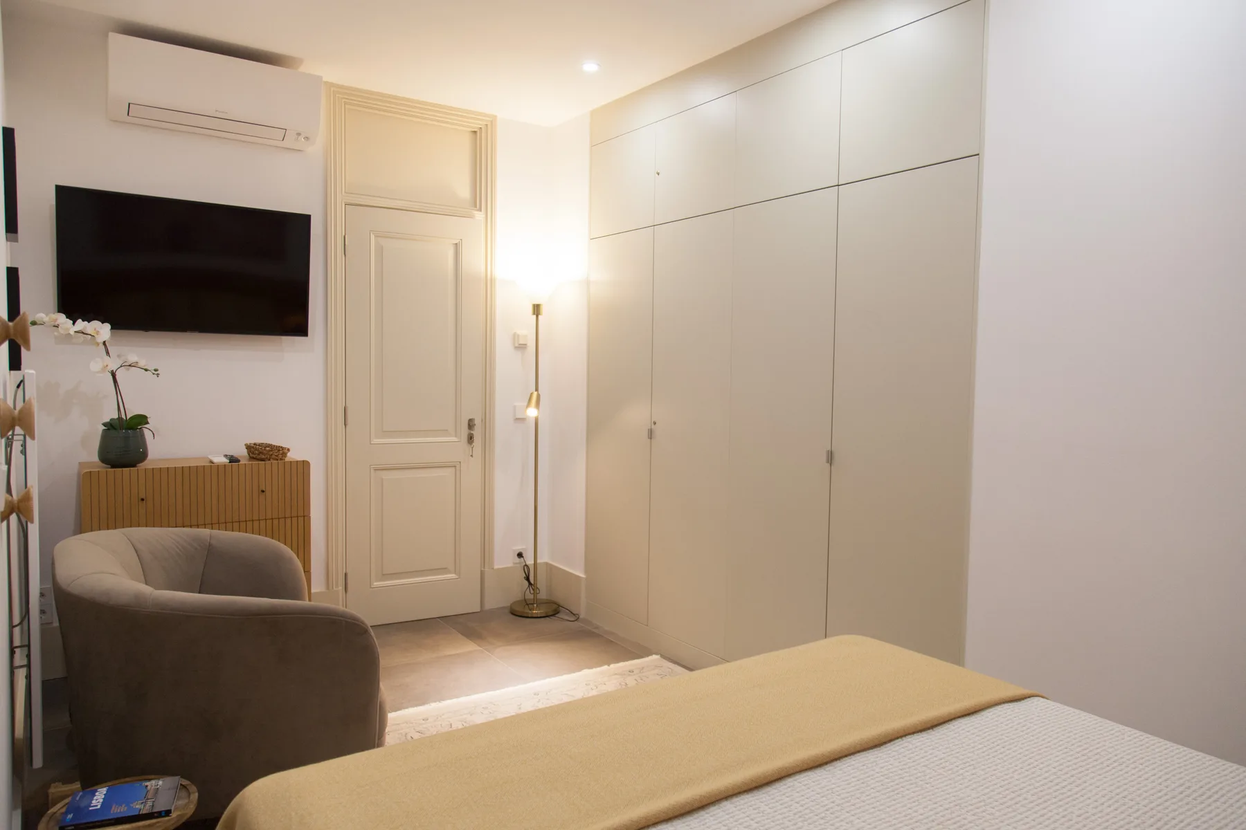 Un dormitorio con una cama, asientos tapizados y un televisor montado en la pared.