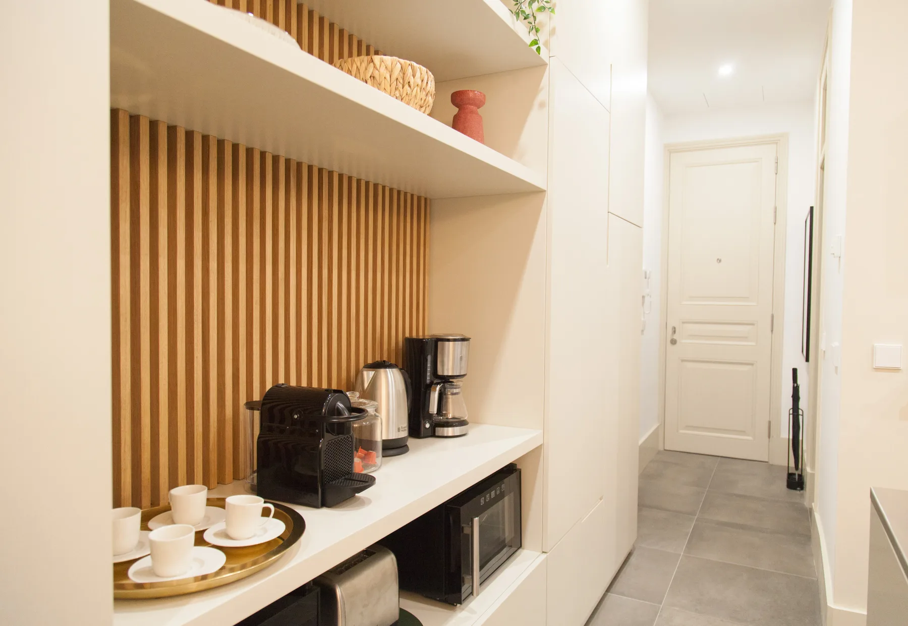 Una encimera de cocina con cafeteras está junto a un pasillo con suelo de baldosas.