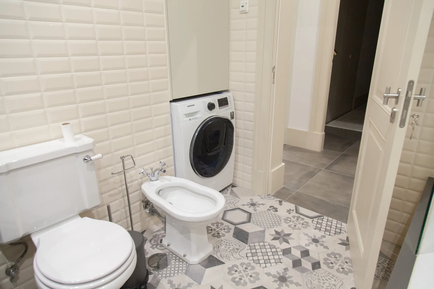 Un baño alicatado con inodoro, bidé y lavadora junto a una puerta abierta.