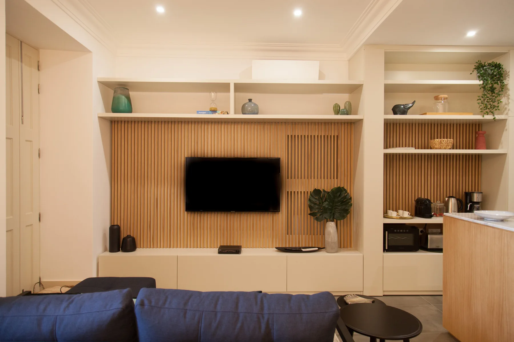 Sala de estar con asientos azules frente a un televisor y estanterías empotradas.