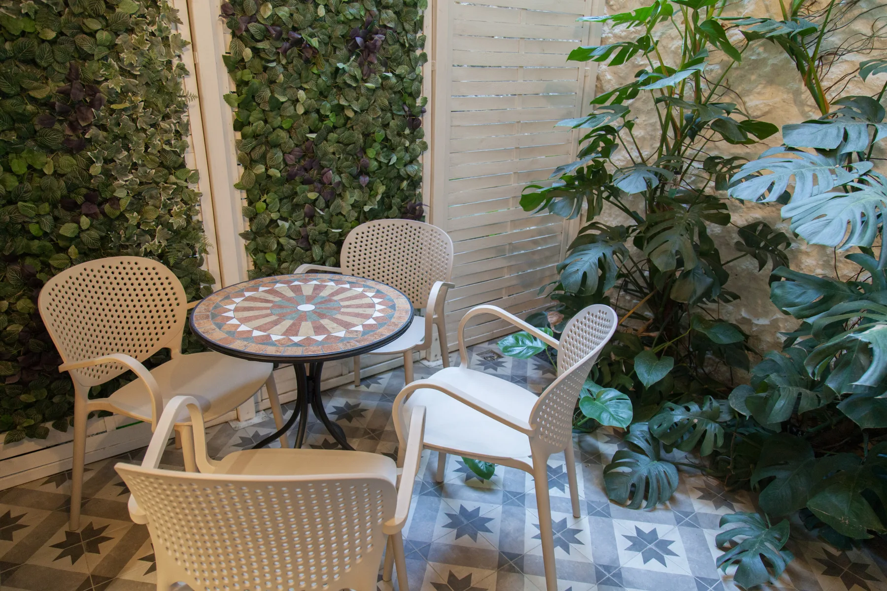 Un patio embaldosado con una mesa redonda y asientos entre plantas frondosas.