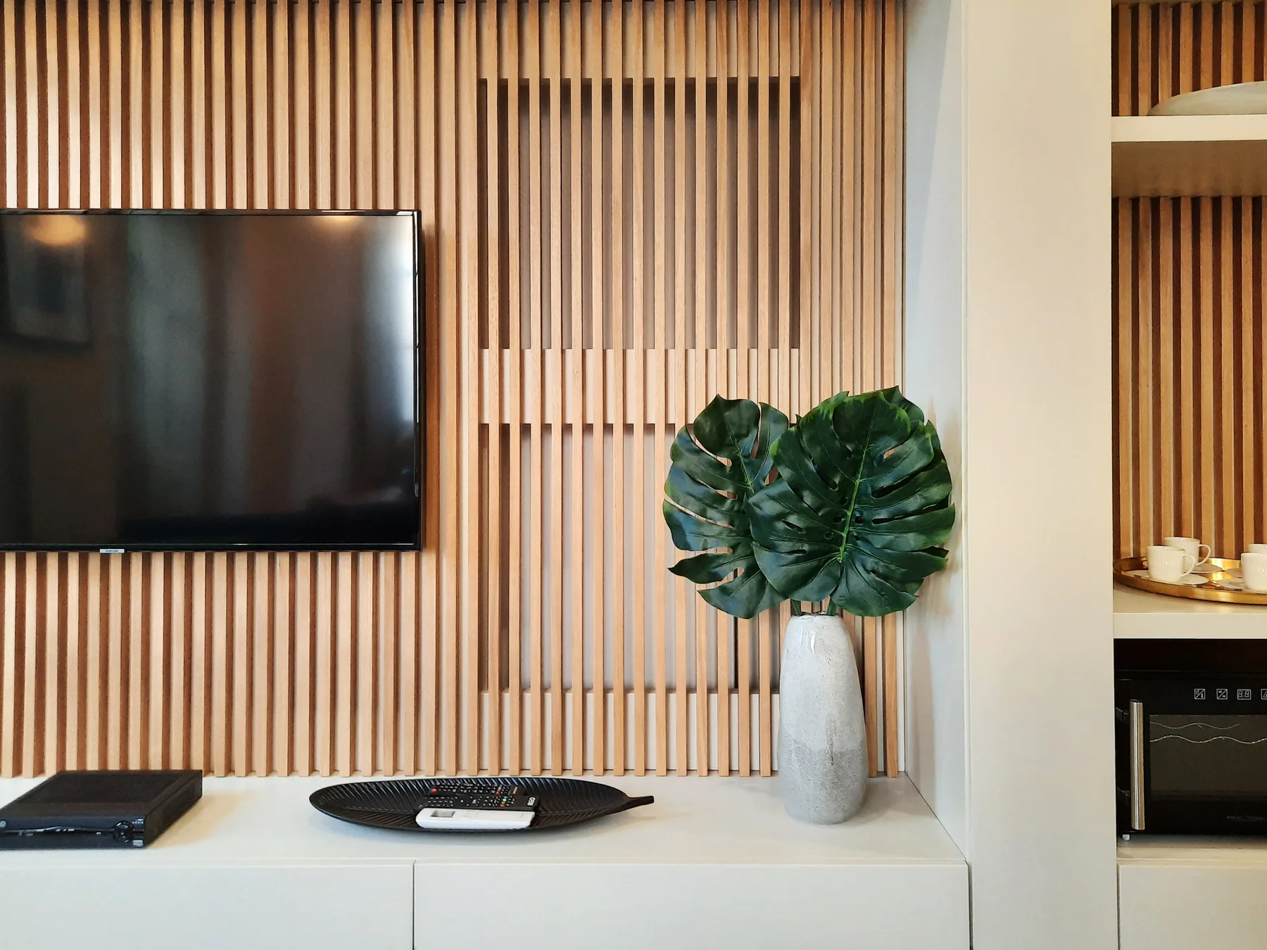 Pared de entretenimiento en una sala de estar con televisión, consola y planta frondosa.