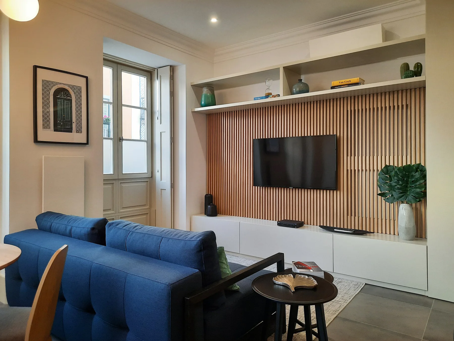 Una sala de estar con asientos azules frente a un televisor y estanterías integradas.