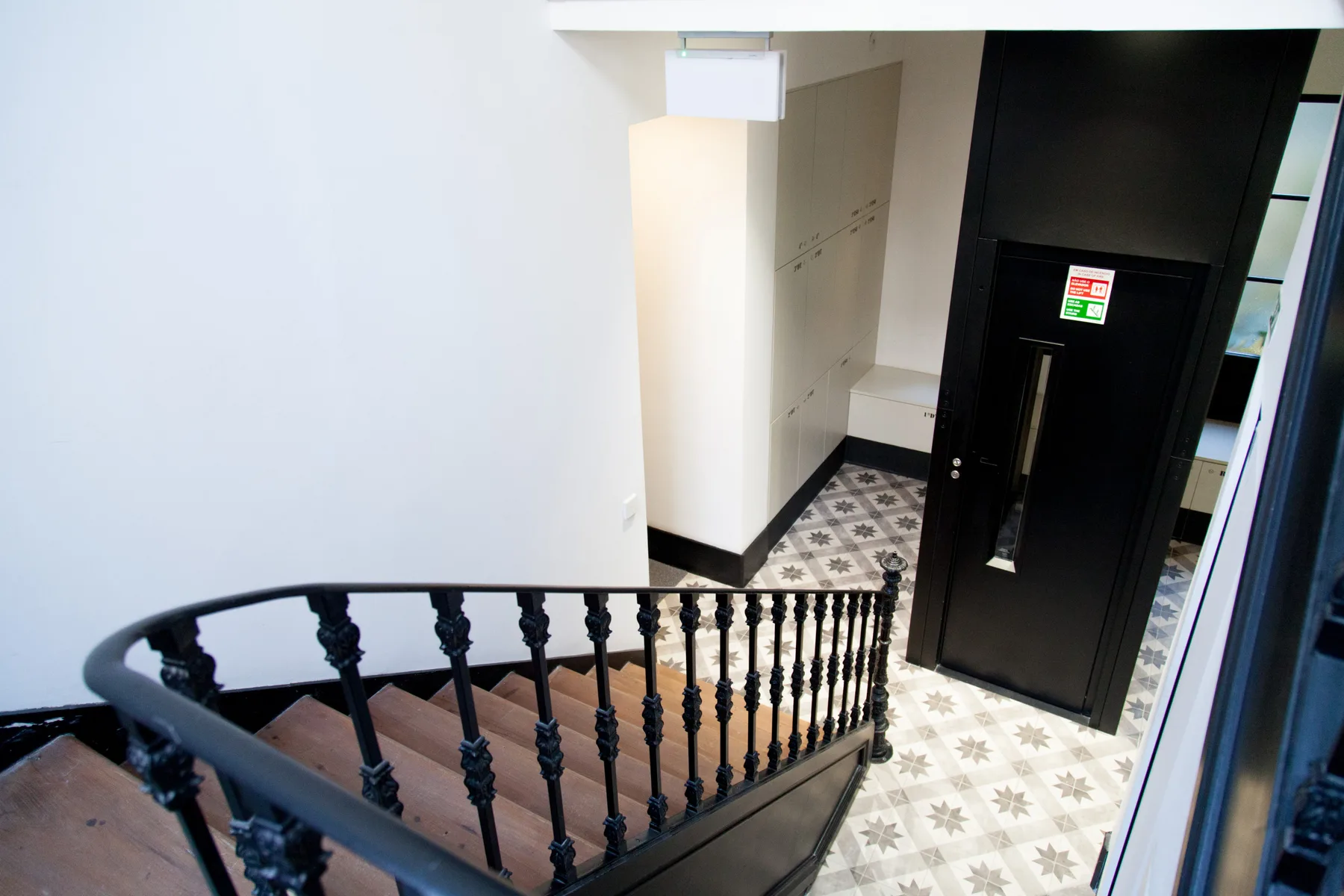 Una escalera interior con barandilla negra y suelo de baldosas estampadas.