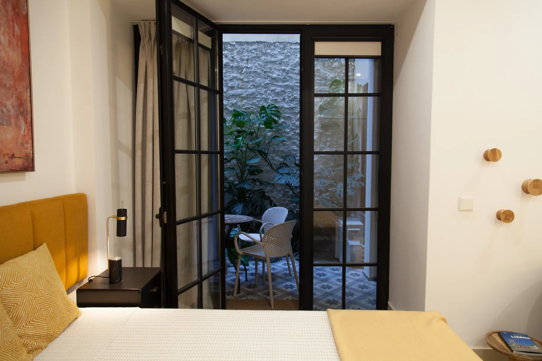 Un dormitorio da a un pequeño patio a través de puertas acristaladas con marcos negros.