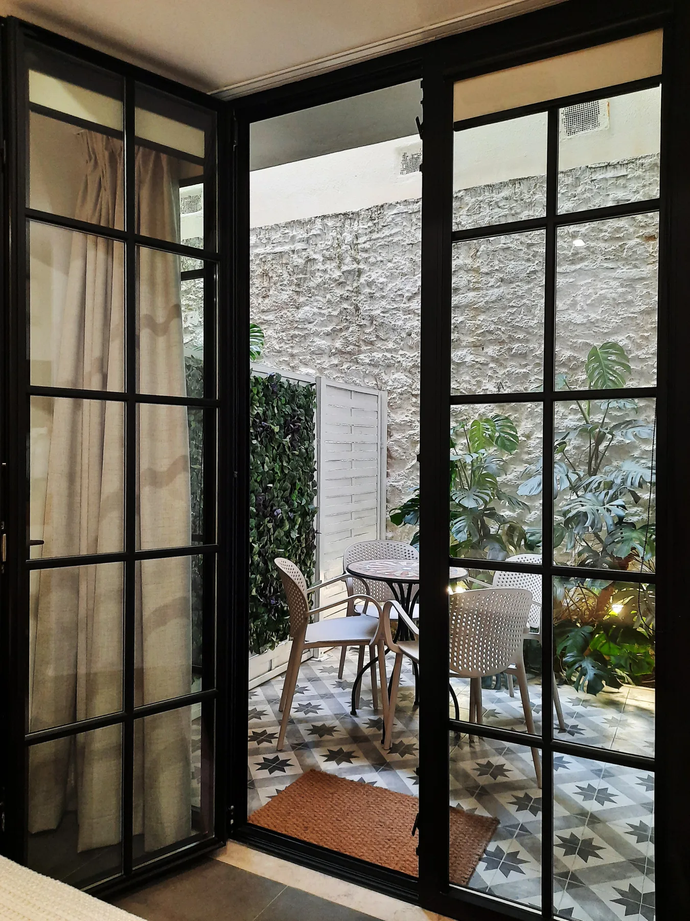 Una pequeña terraza amueblada con asientos y plantas se ve a través de puertas de cristal.