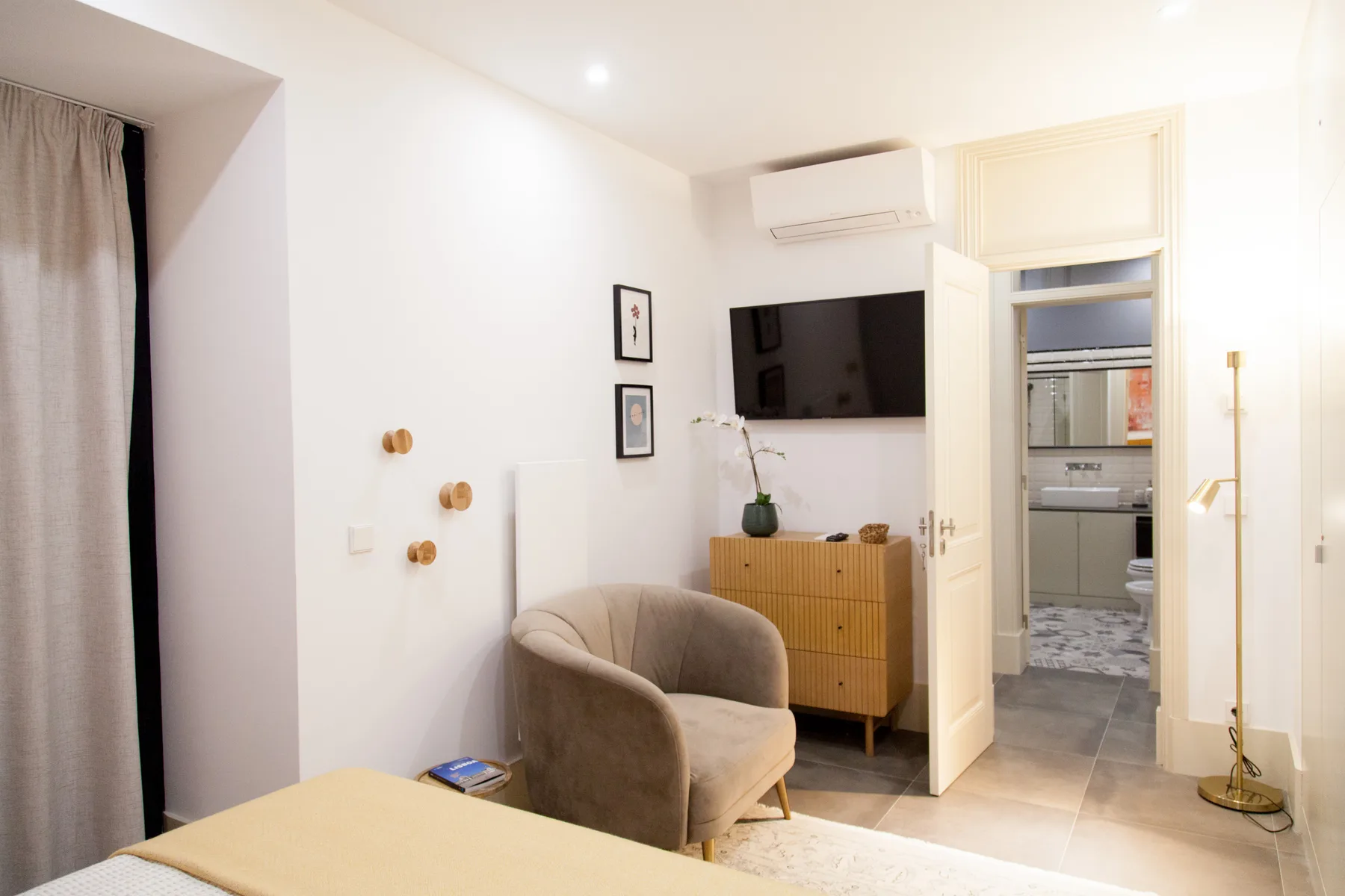 Una sala luminosa tiene un televisor sobre un mueble de madera y un asiento acolchado.