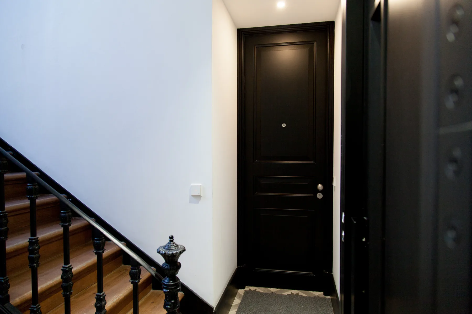 Un recibidor interior con una puerta oscura junto a una escalera.