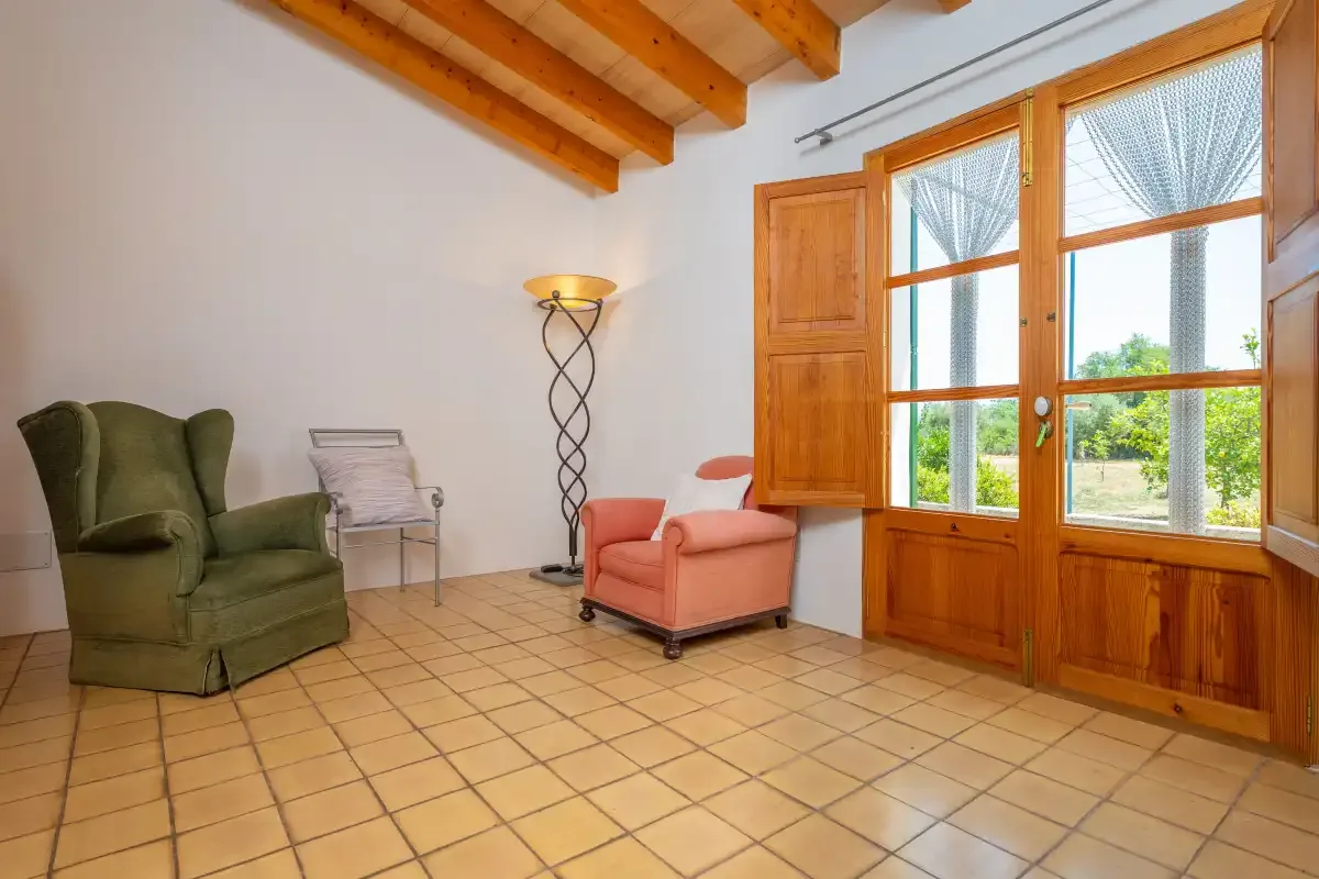 A bright sitting room with armchairs, a floor lamp, and large wooden windows.