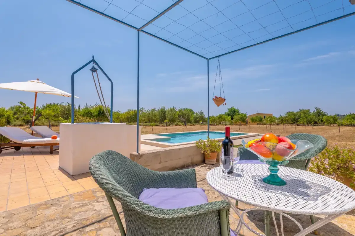 A tiled patio overlooks a swimming pool, with outdoor seating and a fruit bowl.