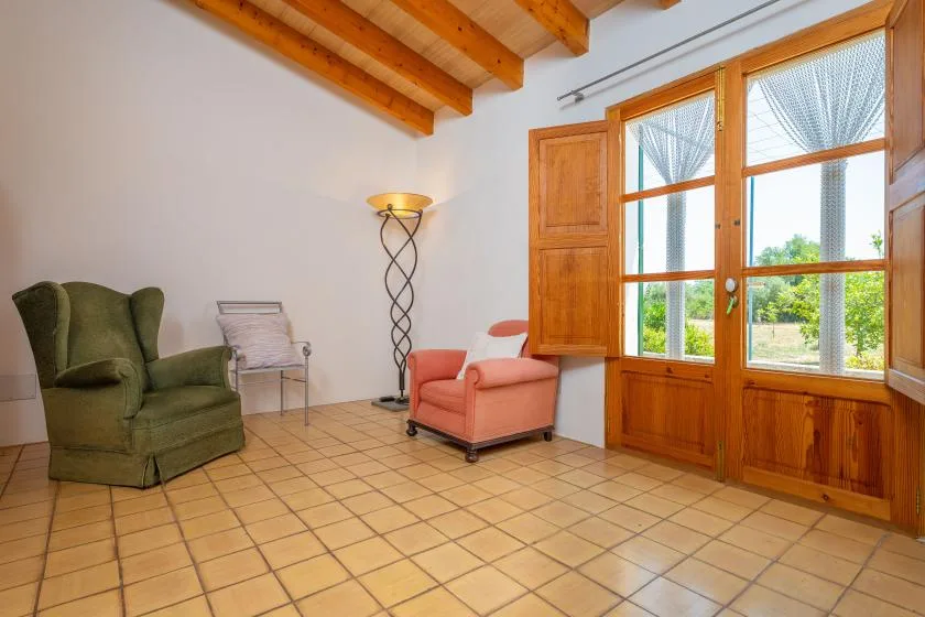 A bright sitting room with armchairs beside large wood-framed windows.