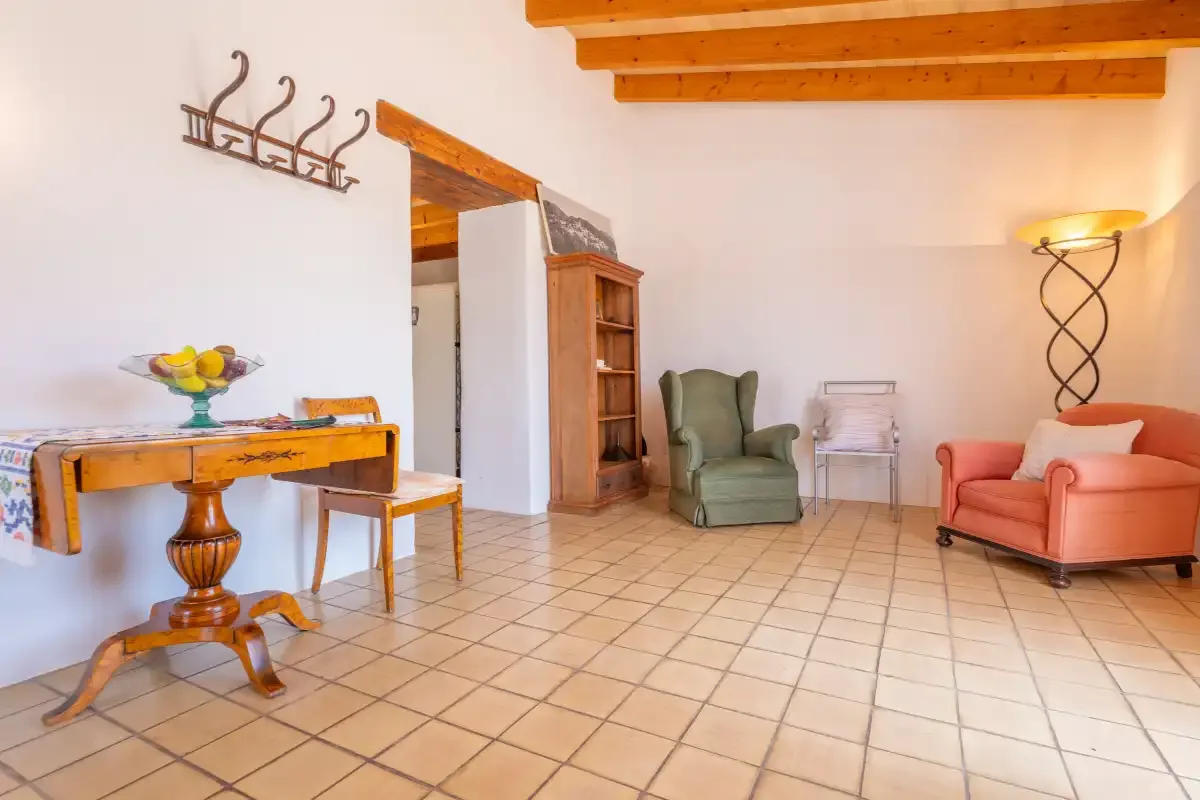 A bright living room with a wooden table, armchairs, and exposed ceiling beams.