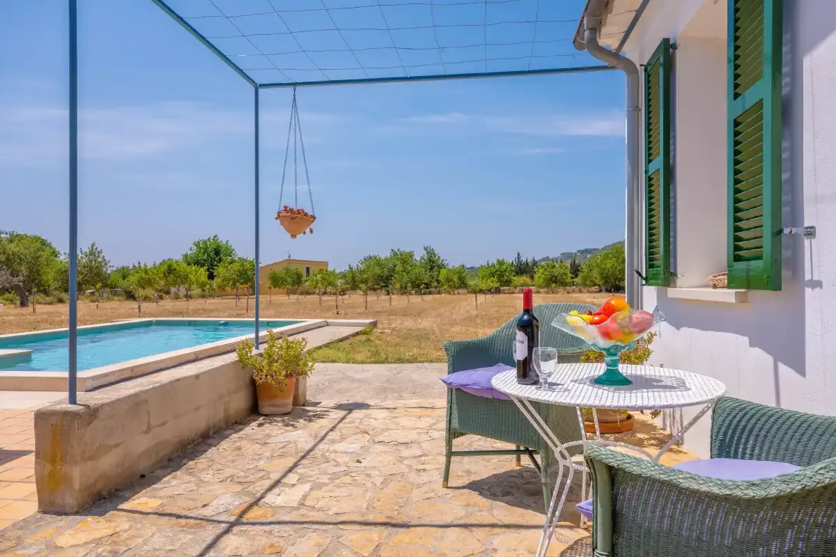 A tiled patio with outdoor seating overlooks a swimming pool and open fields.