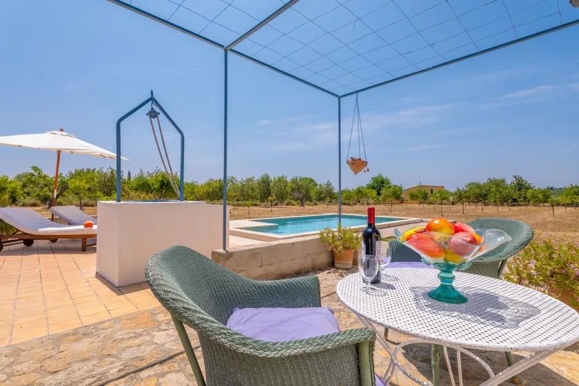 A patio dining area overlooks a swimming pool, with woven seating and a fruit bowl.