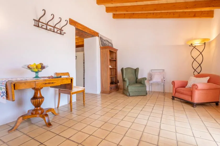 A bright living area with a table, armchairs, and exposed wooden ceiling beams.