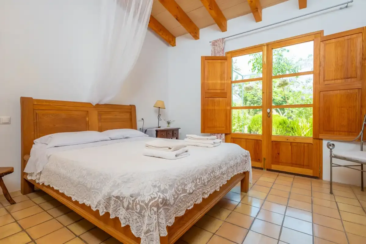 A bedroom with a wooden bed beside open doors to a garden.