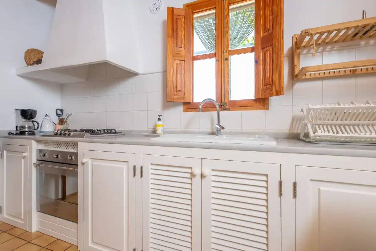 A bright kitchen with white cabinets, a cooktop, and a sink beneath a window.